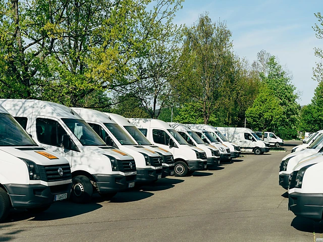A row of white work vans lined up in the sun
